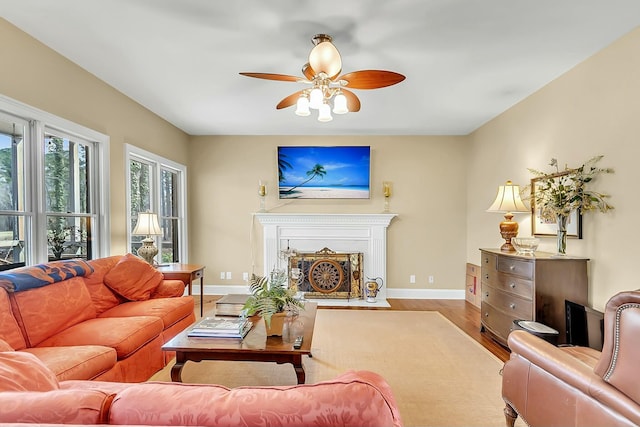 living room featuring wood finished floors, a fireplace with flush hearth, a ceiling fan, and baseboards