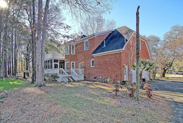 back of house featuring aphalt driveway, an attached garage, brick siding, a sunroom, and crawl space