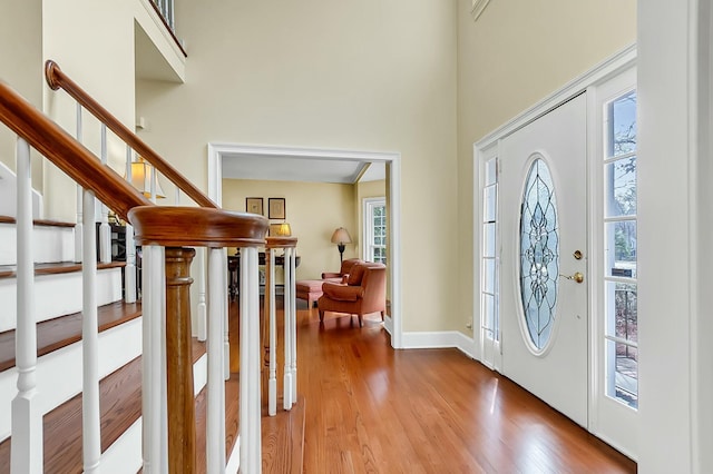 entryway with a towering ceiling, stairs, baseboards, and wood finished floors