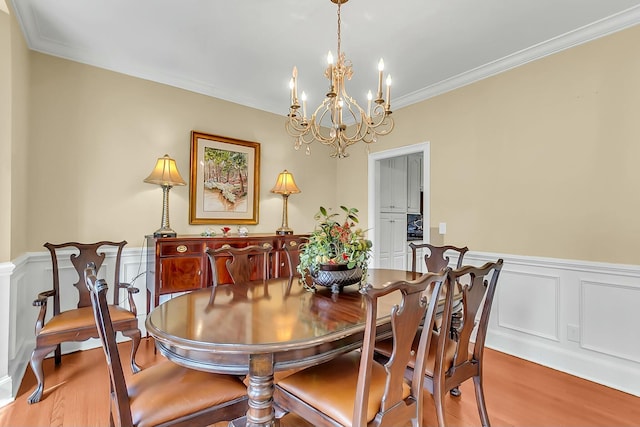 dining room with a wainscoted wall, crown molding, a notable chandelier, and wood finished floors