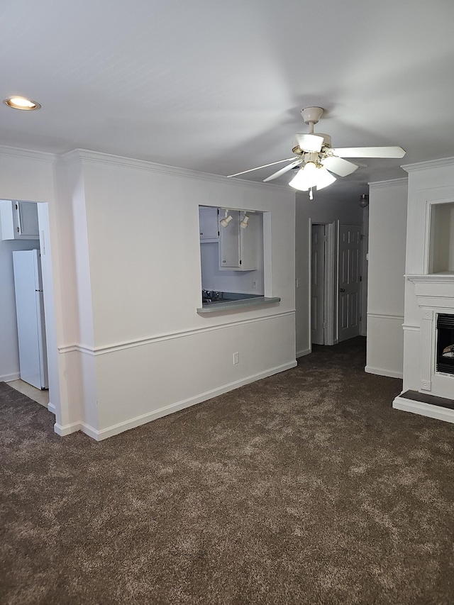 unfurnished living room featuring dark carpet, ceiling fan, and crown molding