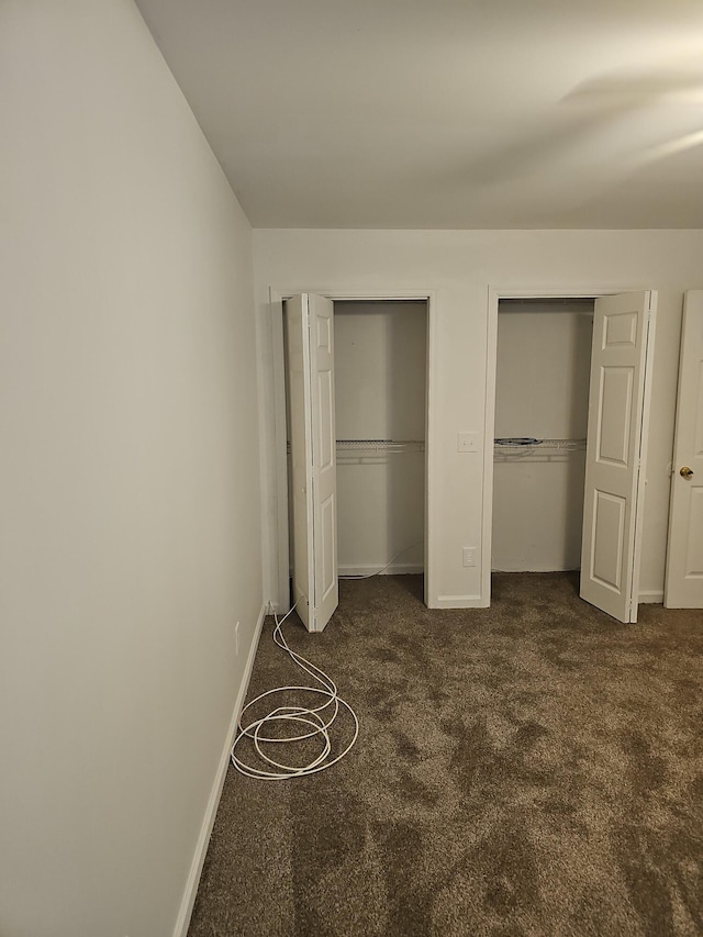 unfurnished bedroom featuring dark colored carpet and multiple closets