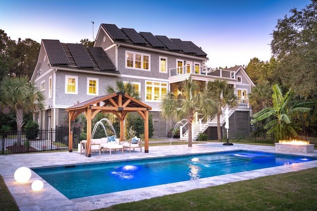 back house at dusk with a gazebo, a patio, solar panels, an outdoor hangout area, and pool water feature