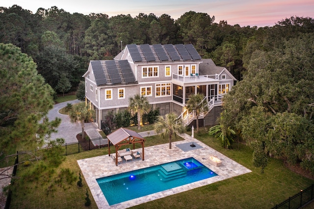 back house at dusk featuring a lawn, a gazebo, solar panels, an outdoor hangout area, and a balcony