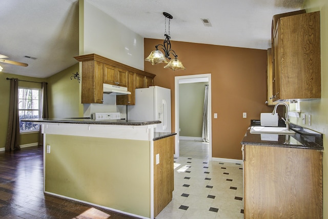 kitchen featuring brown cabinetry, a peninsula, vaulted ceiling, under cabinet range hood, and a sink