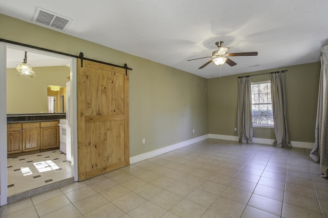 empty room with light tile patterned floors, a barn door, visible vents, baseboards, and a ceiling fan