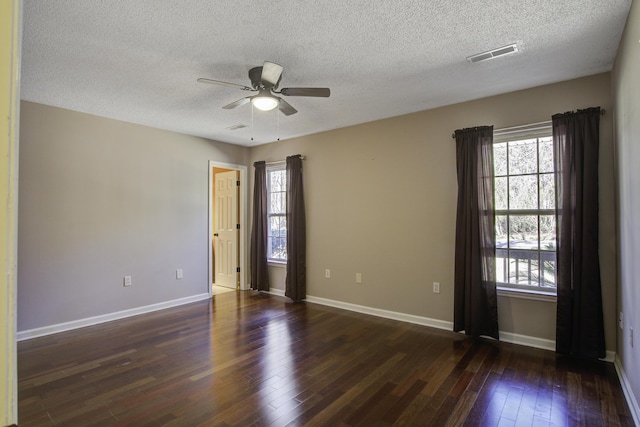 empty room with a wealth of natural light, visible vents, dark wood finished floors, and baseboards