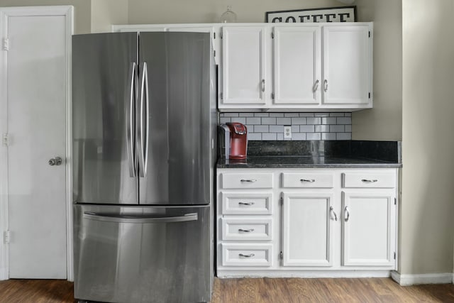 kitchen with tasteful backsplash, freestanding refrigerator, white cabinets, dark stone countertops, and wood finished floors