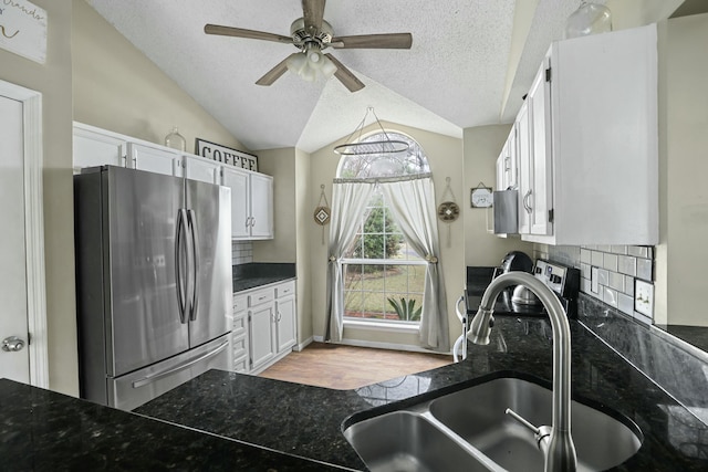 kitchen featuring vaulted ceiling, a sink, freestanding refrigerator, and white cabinets