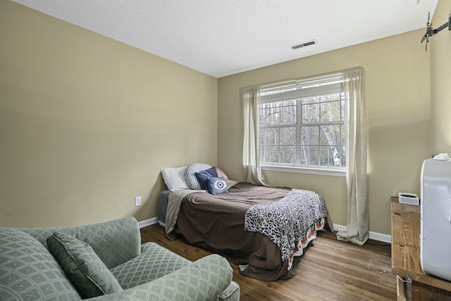 bedroom featuring a textured ceiling, wood finished floors, visible vents, and baseboards