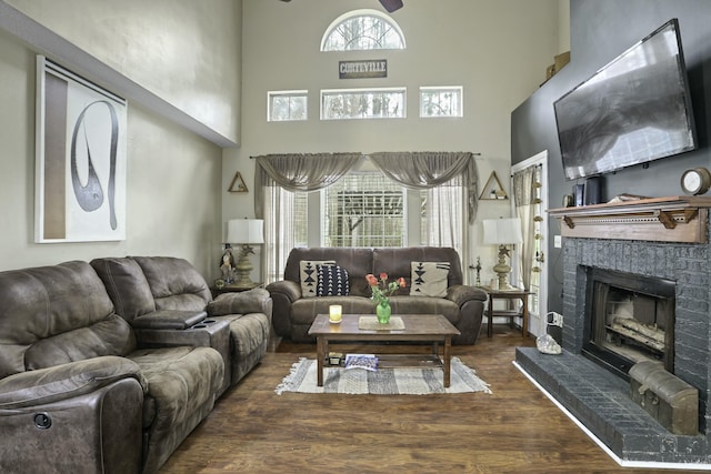 living room featuring a brick fireplace, wood finished floors, and a towering ceiling