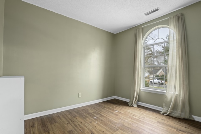 spare room with a healthy amount of sunlight, visible vents, baseboards, and wood finished floors