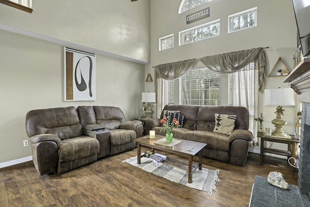 living area with a towering ceiling, baseboards, and wood finished floors