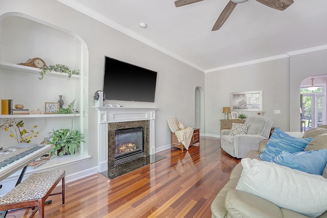 living area featuring crown molding, wood finished floors, a fireplace, arched walkways, and a ceiling fan
