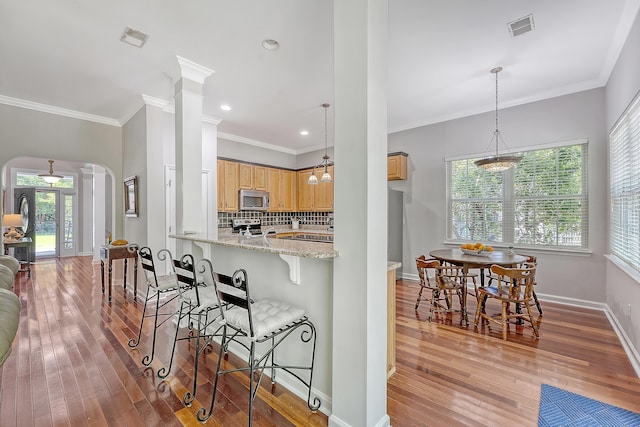 kitchen with arched walkways, stainless steel appliances, light wood-type flooring, and ornate columns