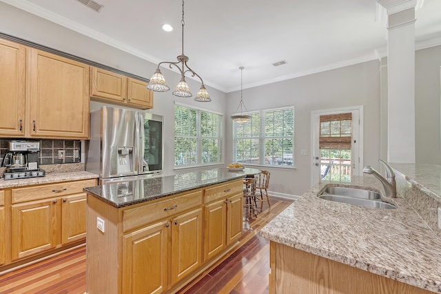 kitchen with a kitchen island, a sink, light stone counters, light wood finished floors, and stainless steel fridge