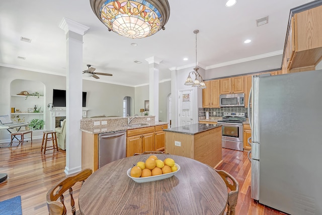 kitchen featuring decorative columns, wood finished floors, a kitchen island, a ceiling fan, and stainless steel appliances