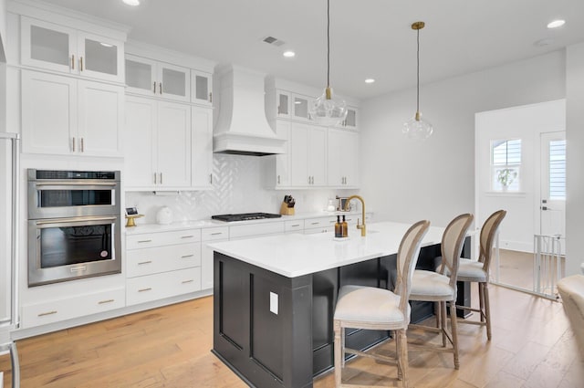 kitchen with double oven, a kitchen bar, light countertops, custom range hood, and white cabinetry