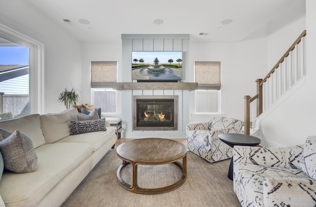 living room featuring a glass covered fireplace, stairs, and visible vents