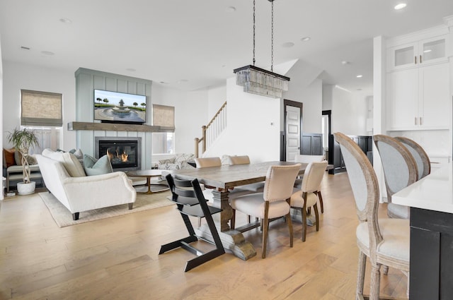 dining space featuring recessed lighting, light wood-type flooring, a glass covered fireplace, and stairway