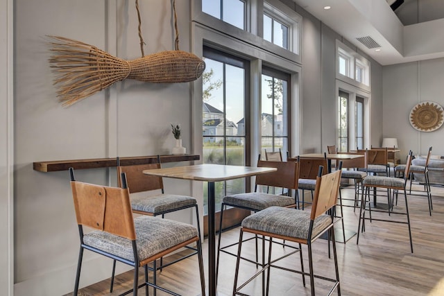 dining area featuring light wood finished floors, visible vents, plenty of natural light, and a towering ceiling