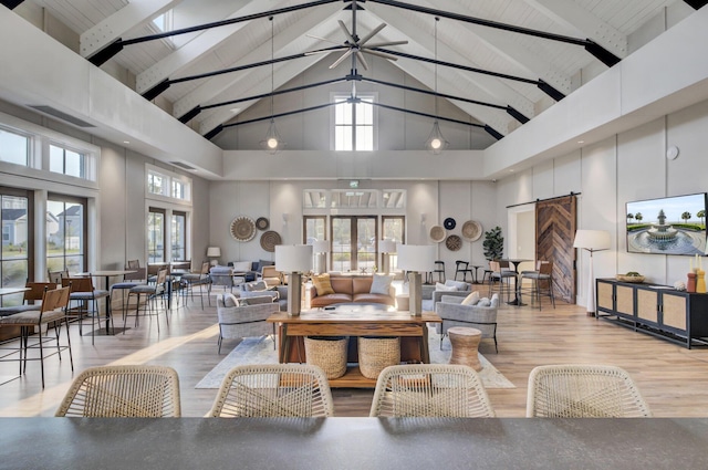 living area with visible vents, wood finished floors, a barn door, and a towering ceiling