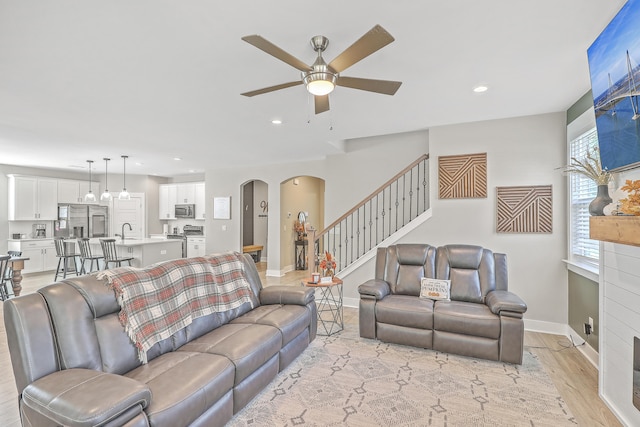 living room with ceiling fan, sink, light wood-type flooring, and a fireplace