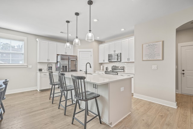 kitchen featuring appliances with stainless steel finishes, light hardwood / wood-style floors, white cabinetry, a kitchen island with sink, and a breakfast bar