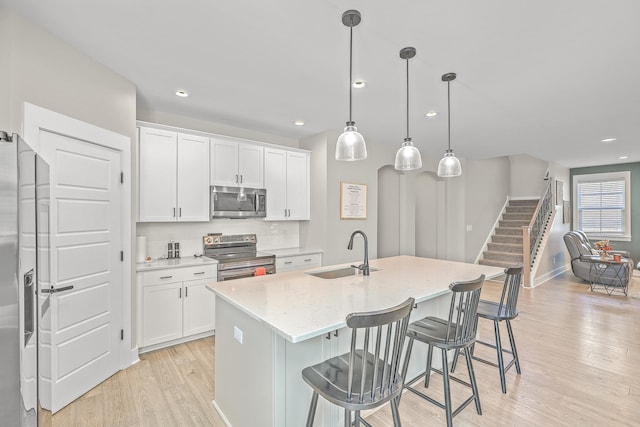 kitchen featuring stainless steel appliances, sink, white cabinets, and a center island with sink