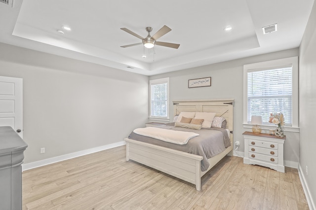 bedroom featuring multiple windows, a tray ceiling, light hardwood / wood-style floors, and ceiling fan