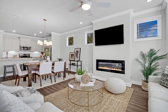 living room with ceiling fan with notable chandelier, dark wood-type flooring, ornamental molding, and sink