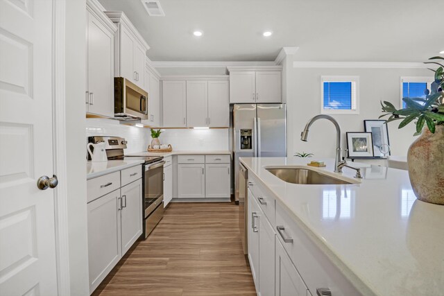 kitchen with ornamental molding, white cabinetry, stainless steel appliances, sink, and light hardwood / wood-style floors