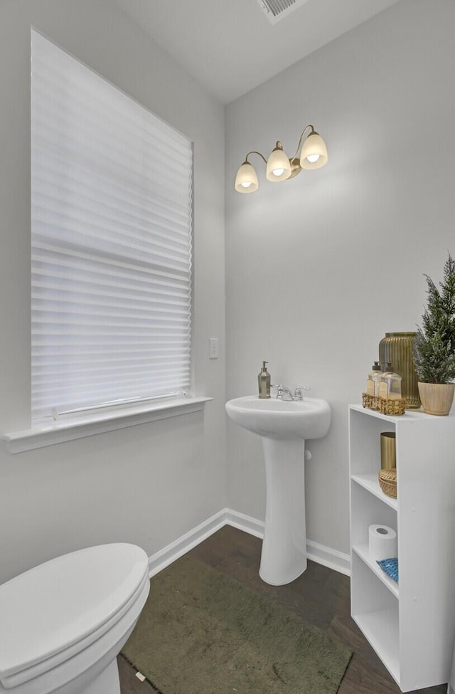 half bath with toilet, baseboards, and wood finished floors