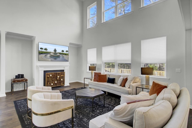 living area featuring a fireplace with flush hearth, a high ceiling, baseboards, and wood finished floors