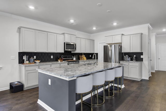 kitchen with dark wood finished floors, a kitchen island with sink, a sink, stainless steel appliances, and a kitchen breakfast bar