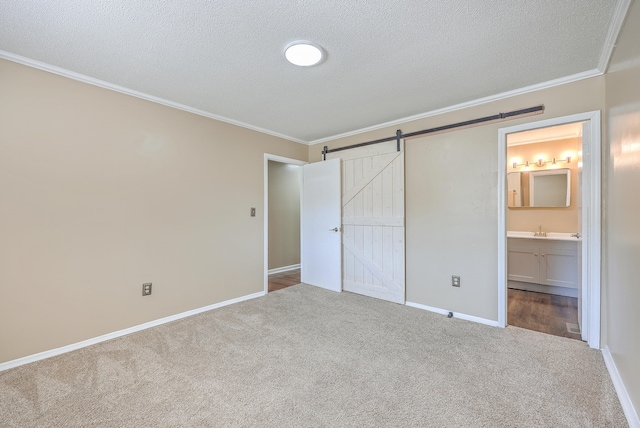 unfurnished bedroom with a barn door, ornamental molding, connected bathroom, and carpet flooring