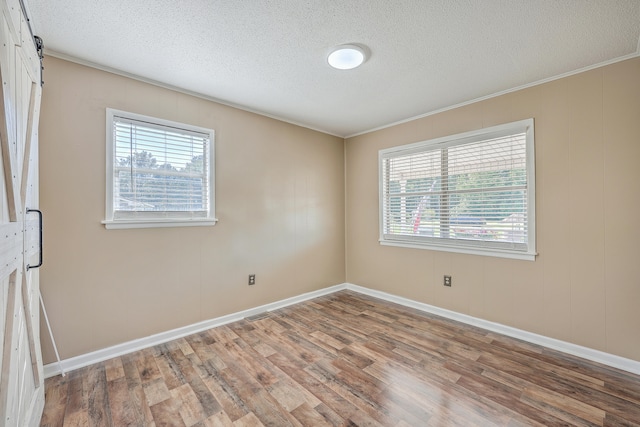 empty room with a barn door, crown molding, a wealth of natural light, and hardwood / wood-style flooring