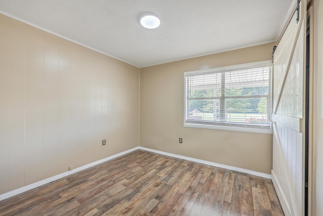 unfurnished room featuring wood-type flooring, crown molding, and a barn door