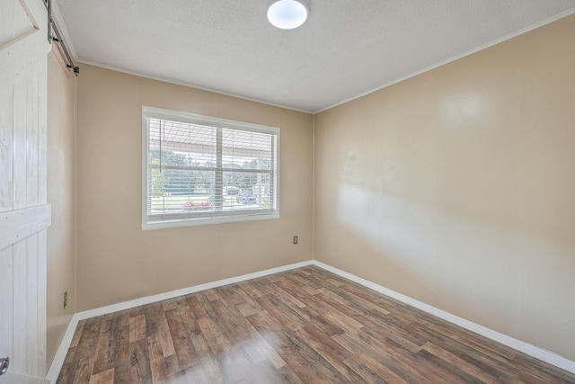 unfurnished room with a barn door, crown molding, a textured ceiling, and dark hardwood / wood-style floors