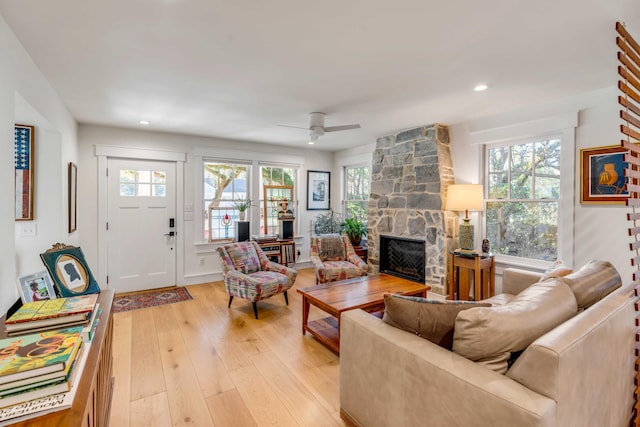 living room with a stone fireplace, light wood-style flooring, recessed lighting, and a wealth of natural light