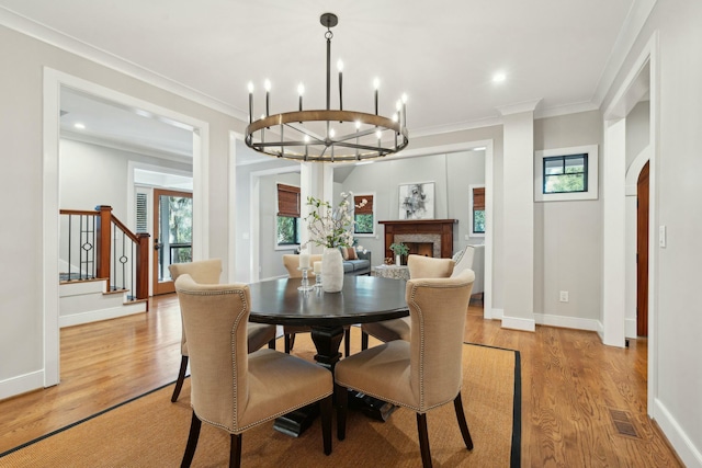 dining room featuring a warm lit fireplace, visible vents, arched walkways, light wood-style flooring, and crown molding