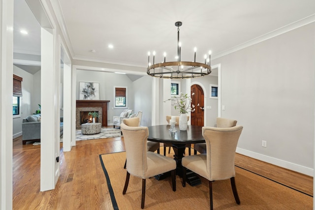 dining space featuring arched walkways, crown molding, light wood finished floors, a warm lit fireplace, and baseboards