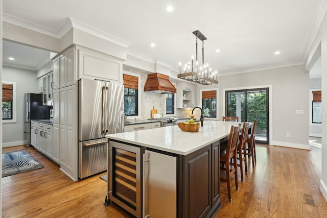 kitchen with premium appliances, wine cooler, light countertops, light wood-style flooring, and backsplash