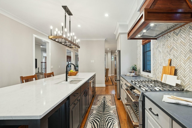 kitchen featuring dark wood finished floors, a center island with sink, custom range hood, appliances with stainless steel finishes, and a sink