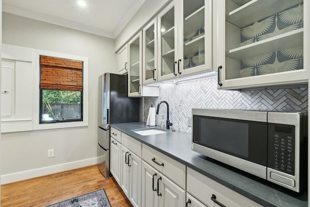 kitchen featuring light wood finished floors, stainless steel appliances, decorative backsplash, ornamental molding, and a sink