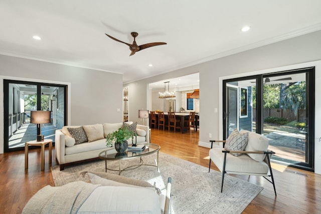 living area with ceiling fan with notable chandelier, crown molding, recessed lighting, and wood finished floors