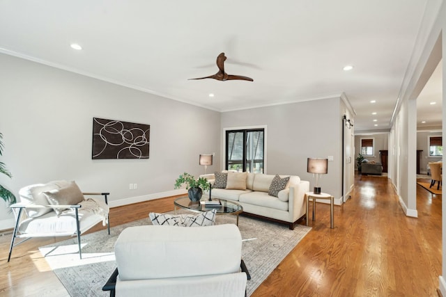 living room with crown molding, a barn door, light wood-style floors, ceiling fan, and baseboards