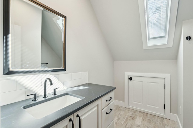 bathroom featuring tasteful backsplash, vanity, wood finished floors, vaulted ceiling with skylight, and baseboards