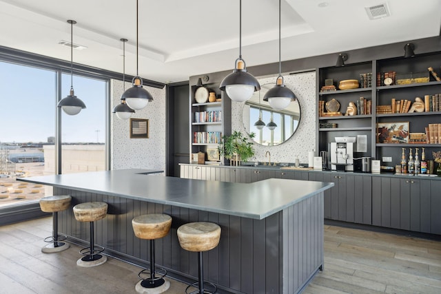 kitchen with tasteful backsplash, hanging light fixtures, light hardwood / wood-style floors, and a raised ceiling