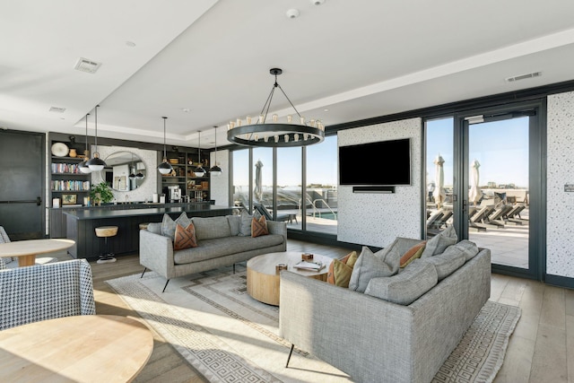 living room featuring bar, light hardwood / wood-style floors, a raised ceiling, and a healthy amount of sunlight